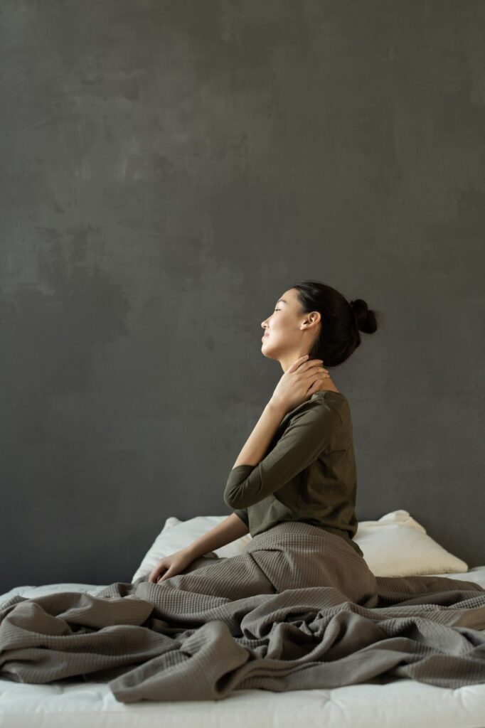 Woman sitting on a bed holding her neck after waking, illustrating morning neck pain