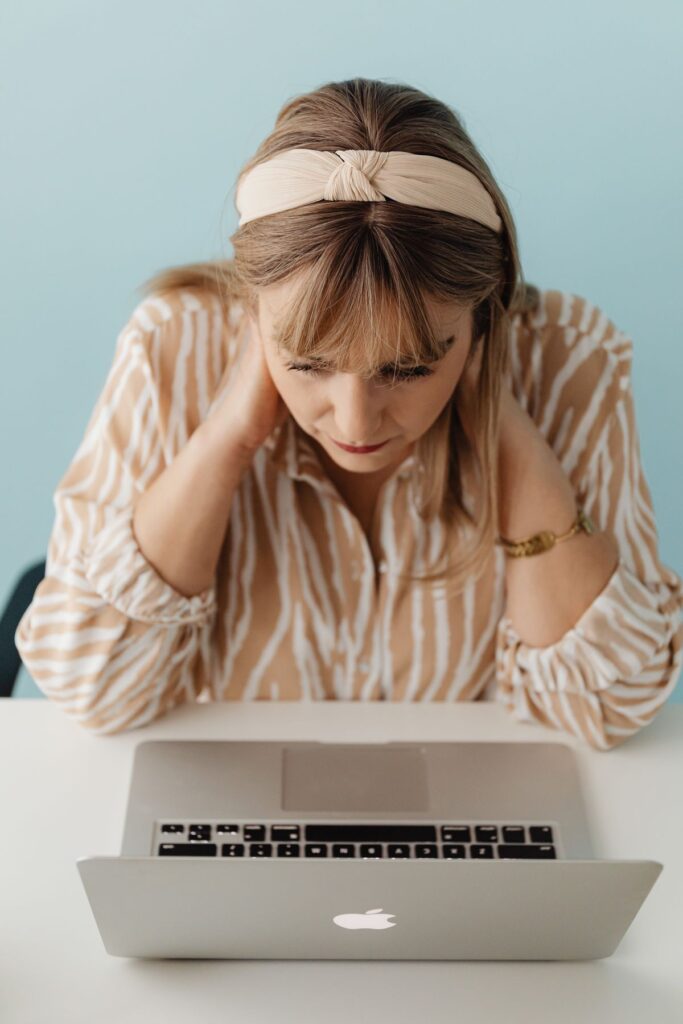 Woman working on a laptop while holding her neck, illustrating tech neck and posture strain