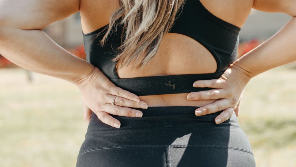 Woman holding her lower back outdoors, illustrating lower back pain and movement