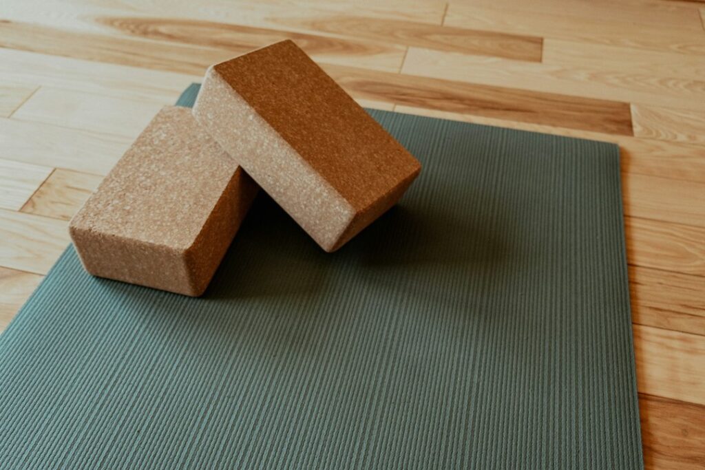 Two cork yoga blocks resting on a green exercise mat on a wooden floor
